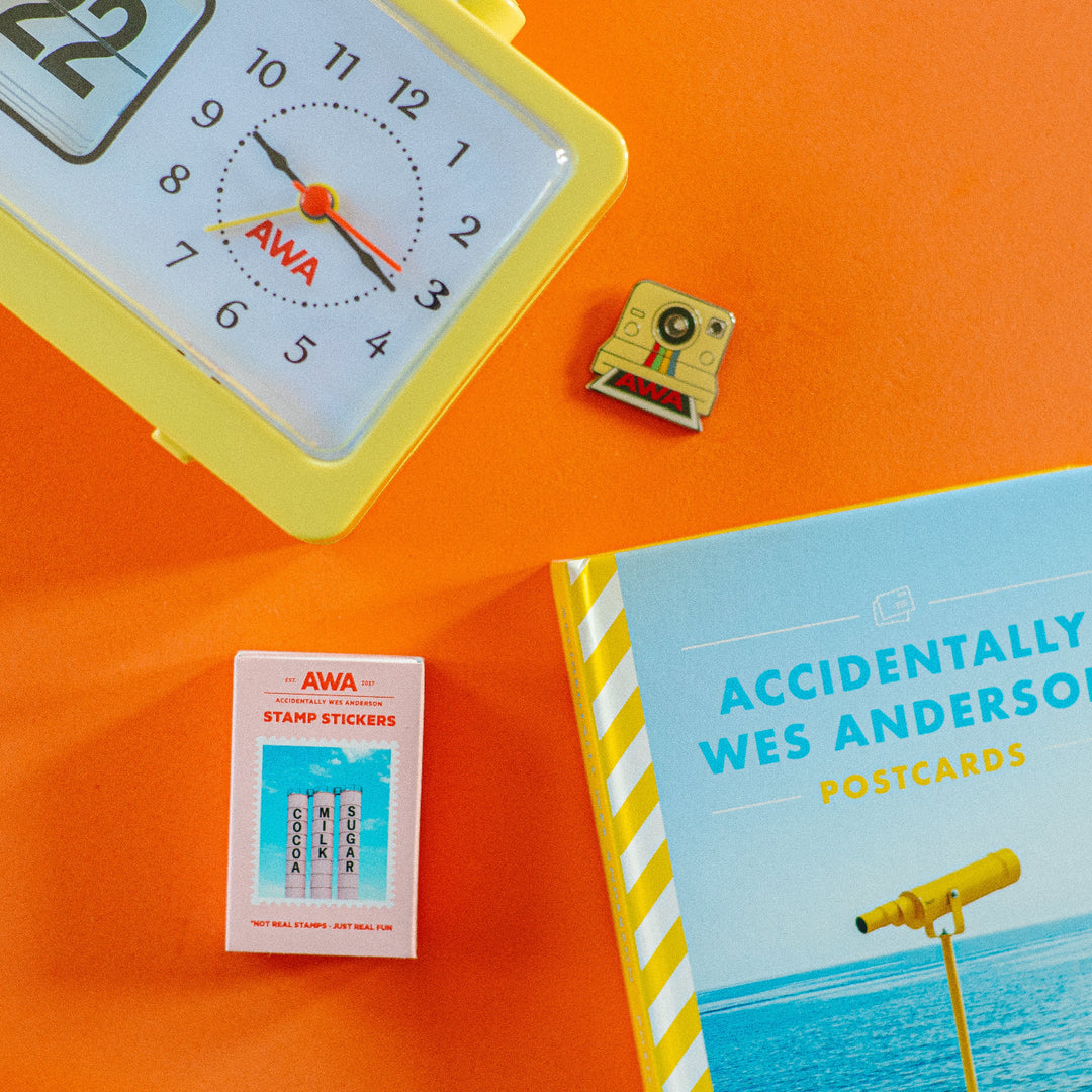 An assortment of items including a yellow analog clock, a book with a polaroid camera illustration, and a set of matchbook stickers with 'AWA' branding.