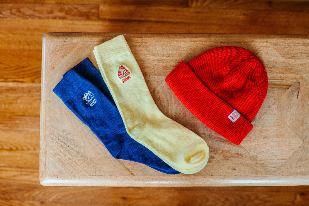 A set of clothing items including yellow socks with a red beanie and blue socks with a camera embroidered on them, placed on a wooden surface.
