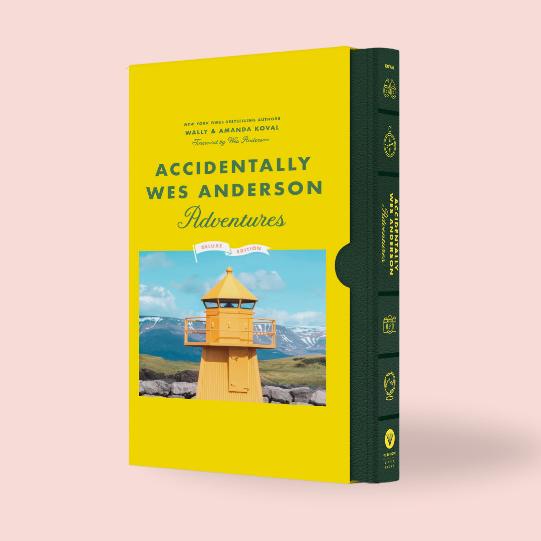 The image shows the hardcover book 'Accidentally Wes Anderson: Adventures' with a yellow and green spine, decorated with a photograph of a lighthouse.