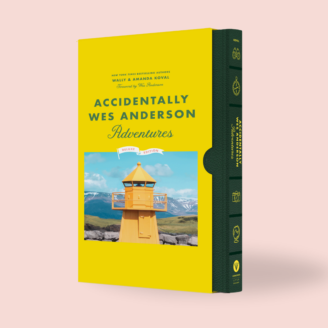 The image shows the hardcover book 'Accidentally Wes Anderson: Adventures' with a yellow and green spine, decorated with a photograph of a lighthouse.
